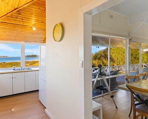 A modern kitchen with a view of the sea, a dining area with a table and chairs, and a balcony with a camera on a tripod.
