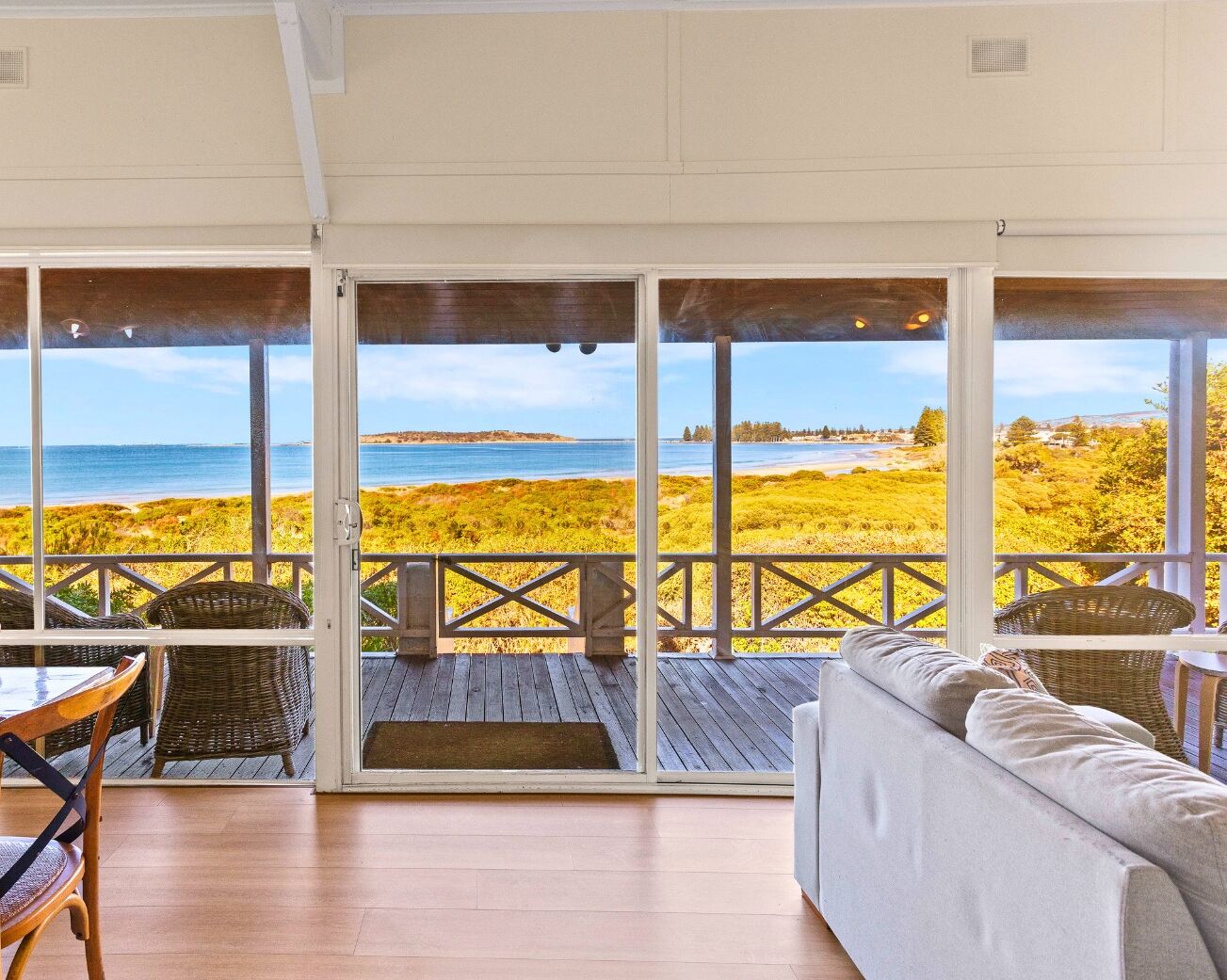 A covered deck with a view of the beach, wicker furniture, and a cushioned seating area.