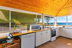 A modern kitchen with large windows, a wooden ceiling, and a view of the sea.