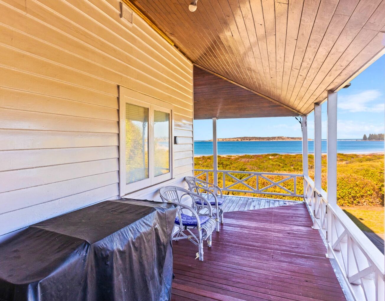 A covered porch with a view of the ocean, featuring a table and two chairs.