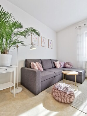A modern living room with a grey sofa, a round coffee table, a potted plant, and framed floral artwork on the wall.