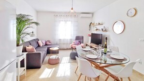 A modern living room with a glass dining table, white chairs, a grey sofa, and a small round ottoman. - Artemis - Markovac Višnjan, cozy apartment with large garden and hot tub (Višnjan)