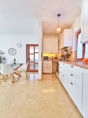 A modern kitchen with white cabinets, a dining area with a round table and chairs, and a visible door leading to another room.