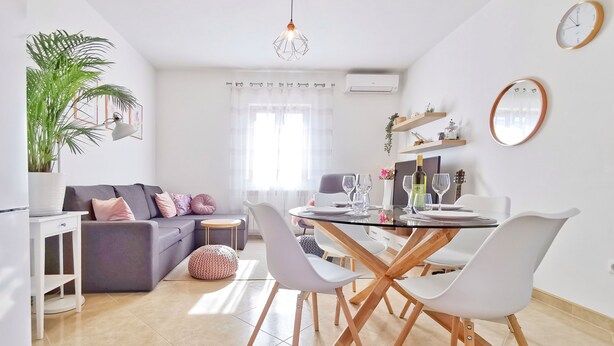 A modern living room with a grey sofa, a dining table with white chairs, a potted plant, and a hanging light fixture. - Artemis - Markovac Višnjan, cozy apartment with large garden and hot tub (Višnjan)