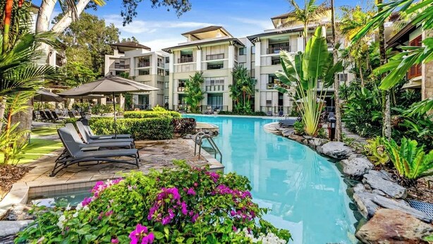 Un hôtel moderne doté d’une piscine, de chaises longues et d’un aménagement paysager de style tropical.
