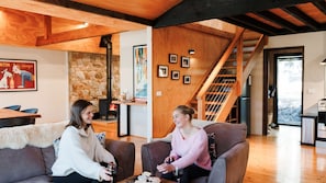 A cozy interior with a stone fireplace, wooden beams, a staircase, and a dining area.