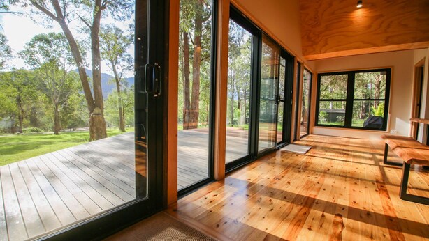 A spacious room with large sliding glass doors leading to an outdoor deck, wooden flooring, and a bench.