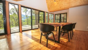 A dining area with a wooden table and chairs, large sliding glass doors, and a view of a forested landscape.