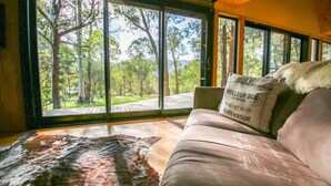 A room with a large window overlooking a forest, a leather couch with a fur throw, and a pillow with text.