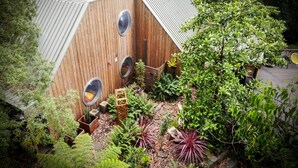 Una cabaña de madera con techo inclinado, rodeada de abundante vegetación y una pequeña terraza.