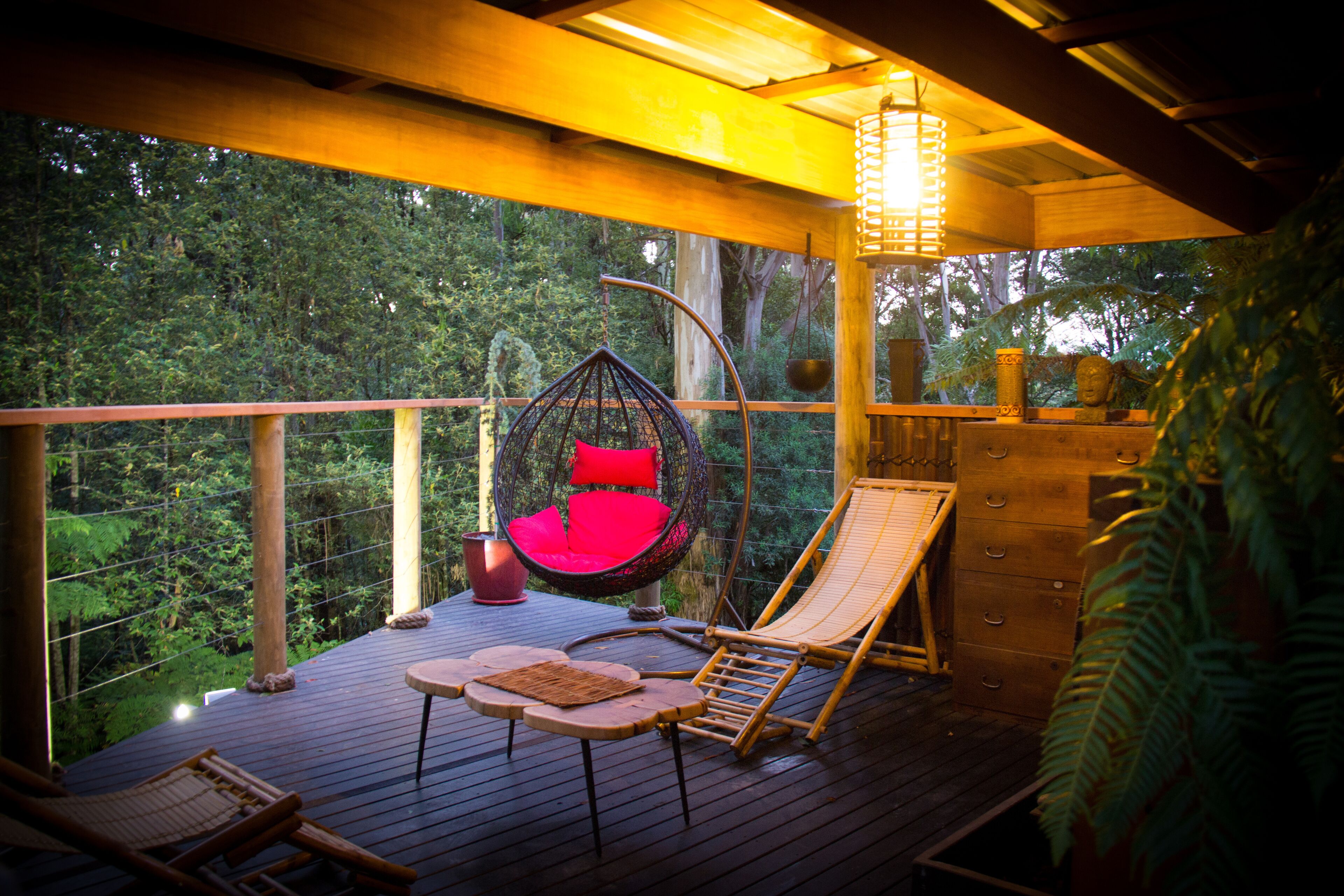 A wooden deck with a hanging chair, a lounge chair, and a table.