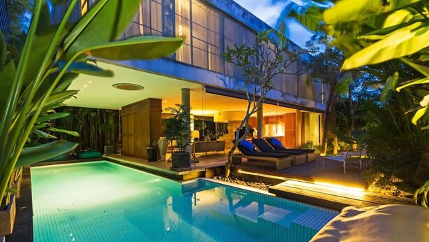 Un'area piscina moderna con una poltrona da relax e un divano, immersa nel verde.