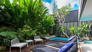 Zona piscina con lettini e un tavolino, circondata da rigogliosa vegetazione tropicale.