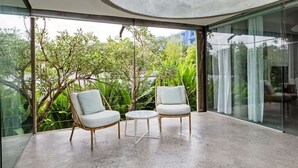 Un interno moderno con due poltrone bianche e un tavolino rotondo, ampie finestre vetrate che offrono vista sul verde circostante.