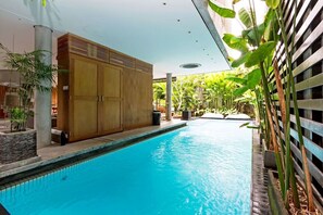 Une piscine dotée d’une terrasse en bois et agrémentée de plantes tropicales.