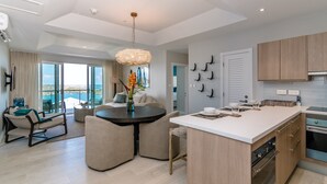 Una cocina moderna con una isla central, un comedor con una mesa redonda y una sala de estar con sofá y vistas al exterior.