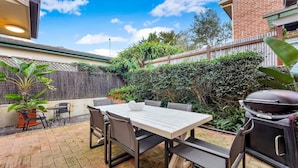 A patio with a table and chairs, a barbecue grill, and a brick wall.
