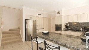 A modern kitchen with white cabinets, a stainless steel refrigerator, a granite countertop, and a microwave.