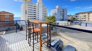 Ein Balkon mit Holztisch und -stühlen mit Blick auf eine Skyline aus hohen Gebäuden und einem klaren Himmel.