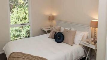 A bedroom with a bed, bedside tables, a window, and a view of greenery.