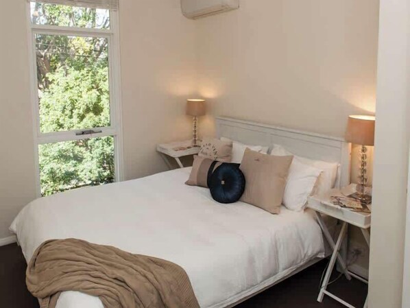 A bedroom with a bed, bedside tables, a window, and a view of greenery.