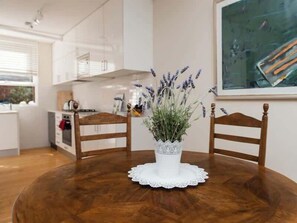 A dining table with a white lace doily, a white vase with lavender, and two wooden chairs.