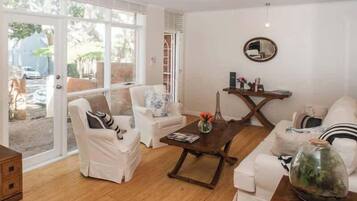 A spacious living room with a large glass door leading to a garden, a round coffee table, and white furniture.