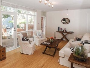 A spacious living room with a large glass door leading to a garden, a round coffee table, and white furniture.
