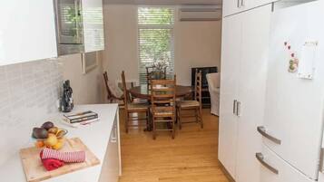 A compact kitchen with white cabinets, a dining table with chairs, a gas stove, and a refrigerator.