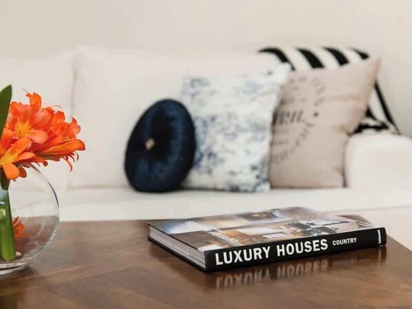A book titled 'Luxury Houses Country' on a wooden table with a vase of orange flowers.