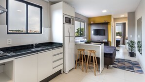A modern kitchen with a built-in microwave, a sink, and a large window. There are two stools and a small island with a countertop. - Pleione Residence (Curitiba)