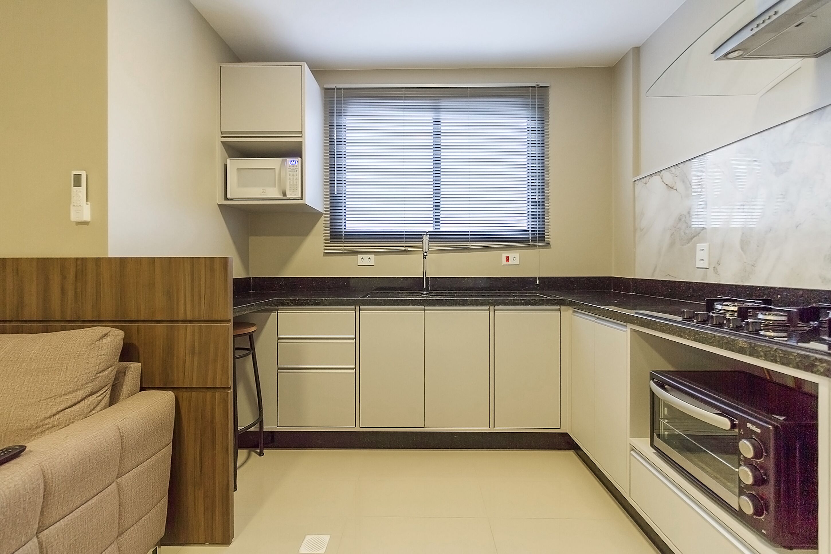 Una cocina compacta con microondas, horno y ventana con persianas.
