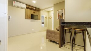 A modern kitchen with a built-in oven, a microwave, and a small refrigerator. There are two stools near the counter and a wooden cabinet above the oven. - Pleione Residence (Curitiba)