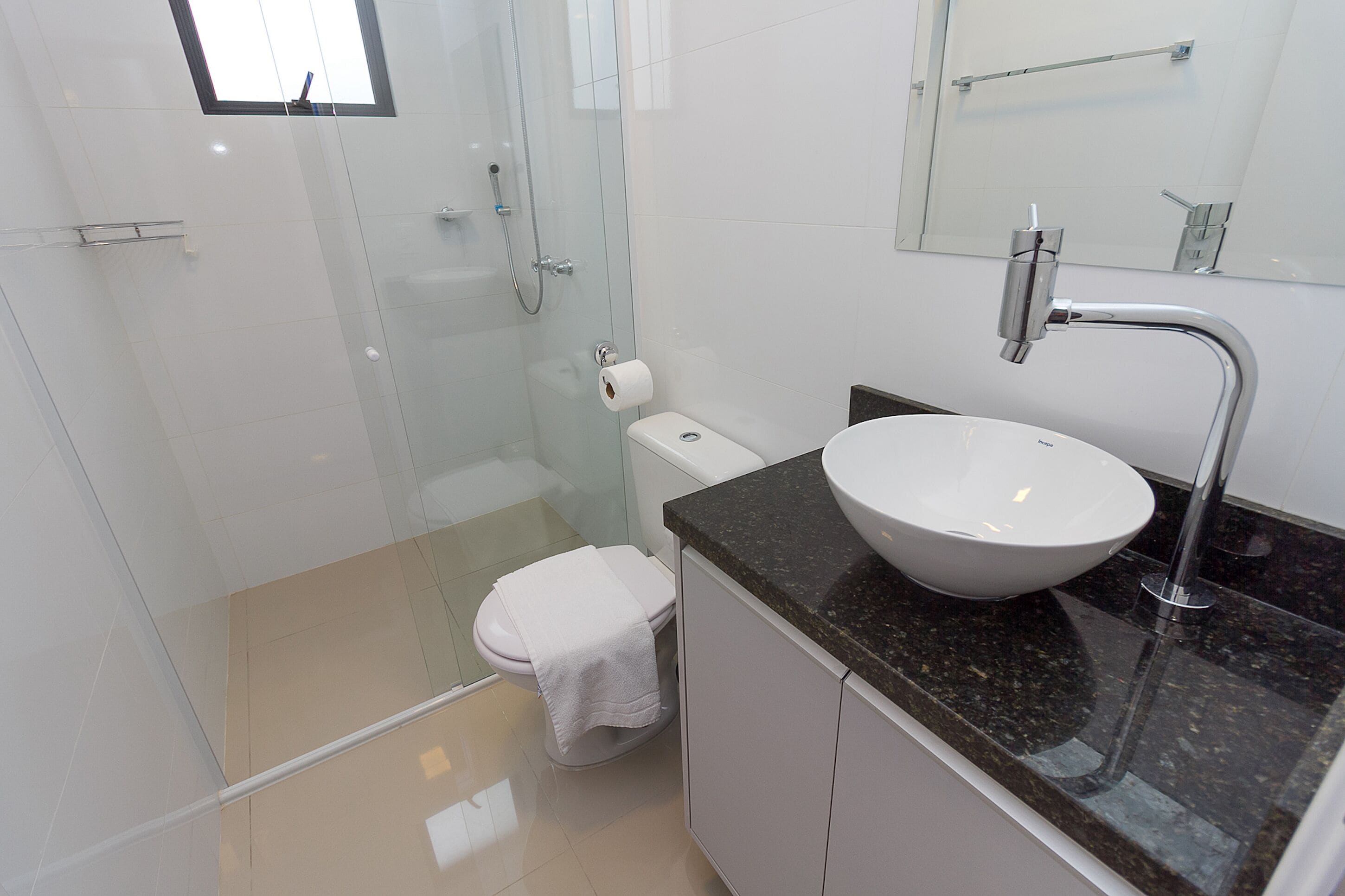 A modern bathroom with a glass shower enclosure, a white toilet, a sink with a marble countertop, and a mirror above the sink.