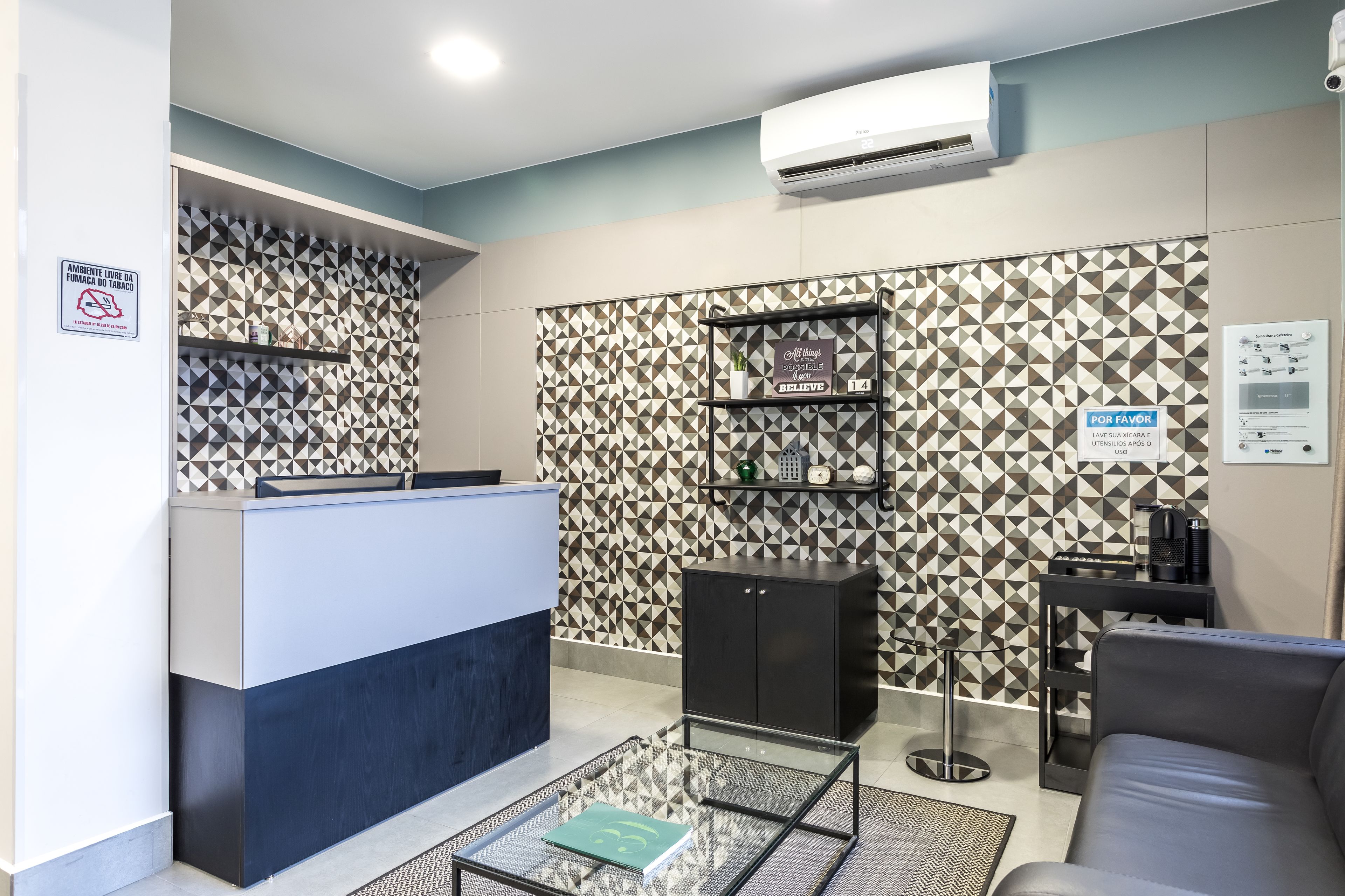 Uma área de recepção com balcão, máquina de café, espaço de estar com sofá e parede estampada.