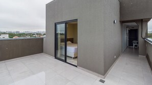 A modern apartment with a balcony, a sliding glass door leading to a bedroom, and a view of the cityscape. - Pleione Residence (Curitiba)