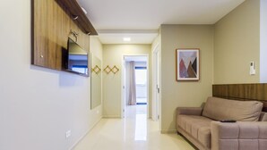 A hallway with a sofa, a TV mounted on the wall, and a framed picture on the wall. - Pleione Residence (Curitiba)