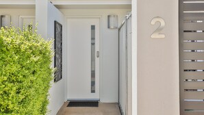 Une entrée moderne avec une porte blanche, une plaque portant le numéro « 2 » et un portail en métal.