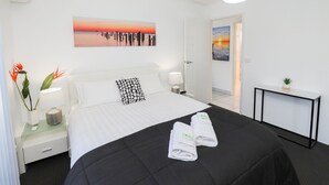 Une chambre d’hôtel avec un lit, des tables de chevet, une commode, un bureau et un tableau au mur.