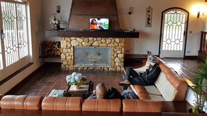 Een gezellige woonkamer met een stenen openhaard, een leren bank en een televisie bevestigd aan een houten balk boven de openhaard.
