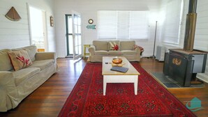 Una sala de estar con un sofá color beige, un tapete de diseño rojo, una mesa de centro y un estufa de leña.