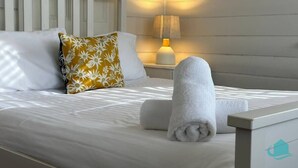 Una cama bien hecha con sábanas blancas, un cojín floral y toallas enrolladas.