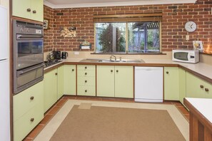 A kitchen with green cabinets, a brick wall, a window, a sink, a microwave, and a dishwasher. - Jazz’s Leafy Retreat: Warm and welcoming family home. Walk to beach and town! (Dunsborough)
