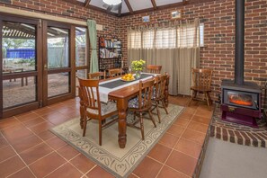 A dining area with a brick wall, a wooden table, chairs, a bookshelf, and a fireplace. - Jazz’s Leafy Retreat: Warm and welcoming family home. Walk to beach and town! (Dunsborough)