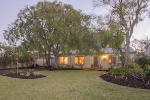 A two-story house with a covered patio, surrounded by a well-maintained lawn and mature trees. - Jazz’s Leafy Retreat: Warm and welcoming family home. Walk to beach and town! (Dunsborough)