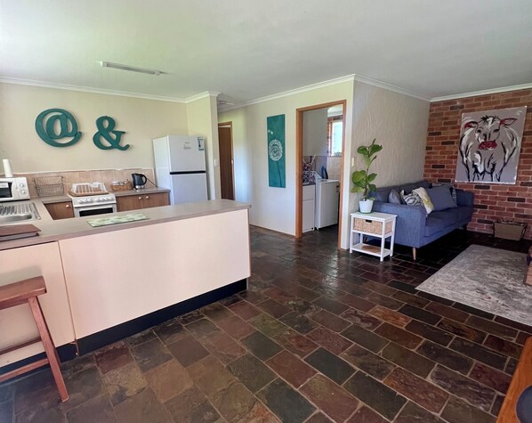 A modern kitchen with a central island, a dining area with a blue sofa, and a living room with a brick wall and artwork.