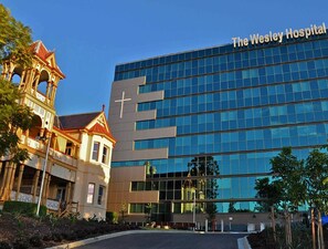 Standing alongside a traditional building, The Wesley features a striking glass facade with a prominent cross.