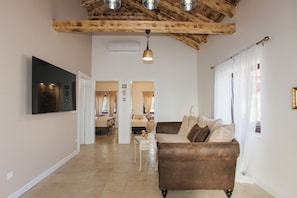 A spacious living area with a brown sofa, a white coffee table, and a TV mounted on the wall.