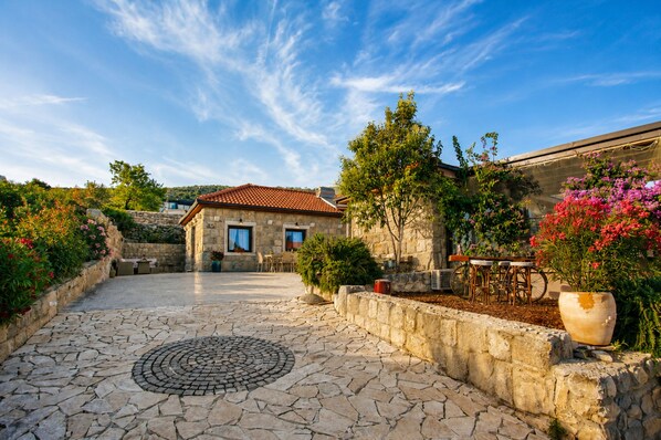 A courtyard with stone flooring, a small building with a tiled roof, and potted plants.