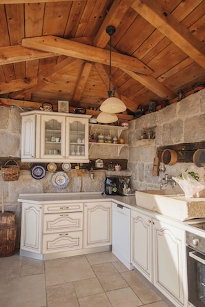 A rustic kitchen with wooden beams, white cabinetry, and stone walls.